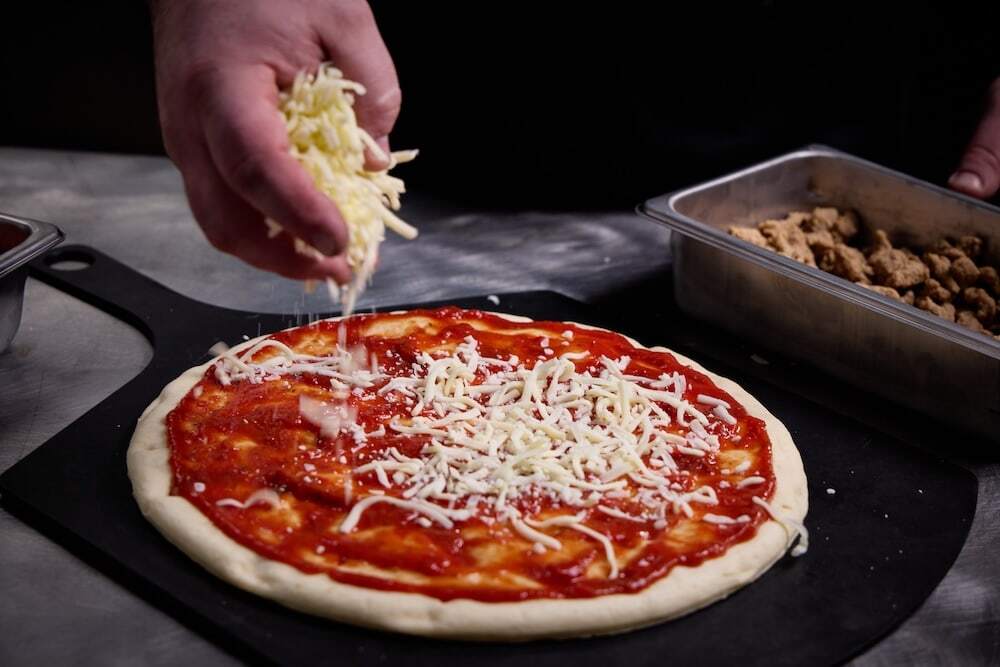 spreading cheese on a hand tossed pizza