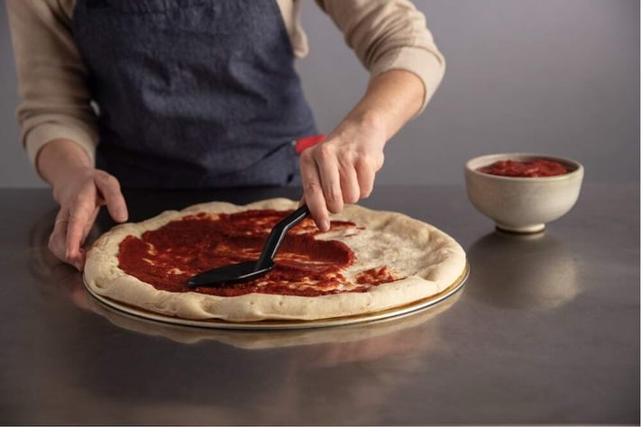spreading sauce on a fresh pizza crust