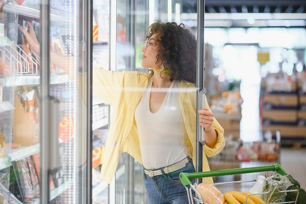 woman reaching for frozen pizza in a grocery store