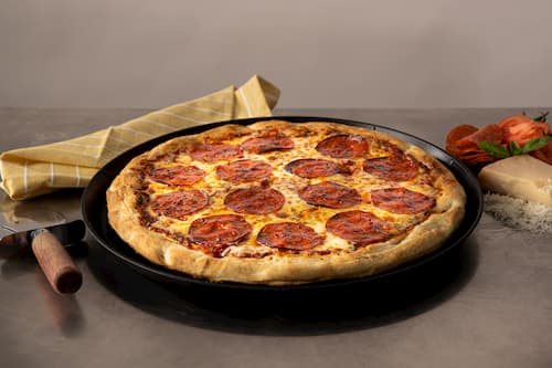 Pepperoni pizza sitting on pizza pan next to pizza cutter